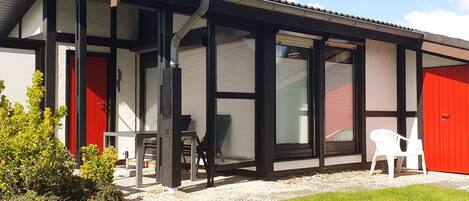 A modern building with large windows, a red door, and a covered outdoor area with chairs.
