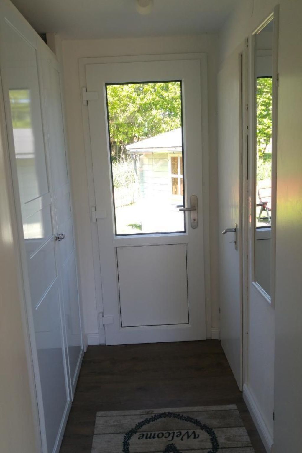 A white door with a small window, a welcome mat, and a wooden floor.