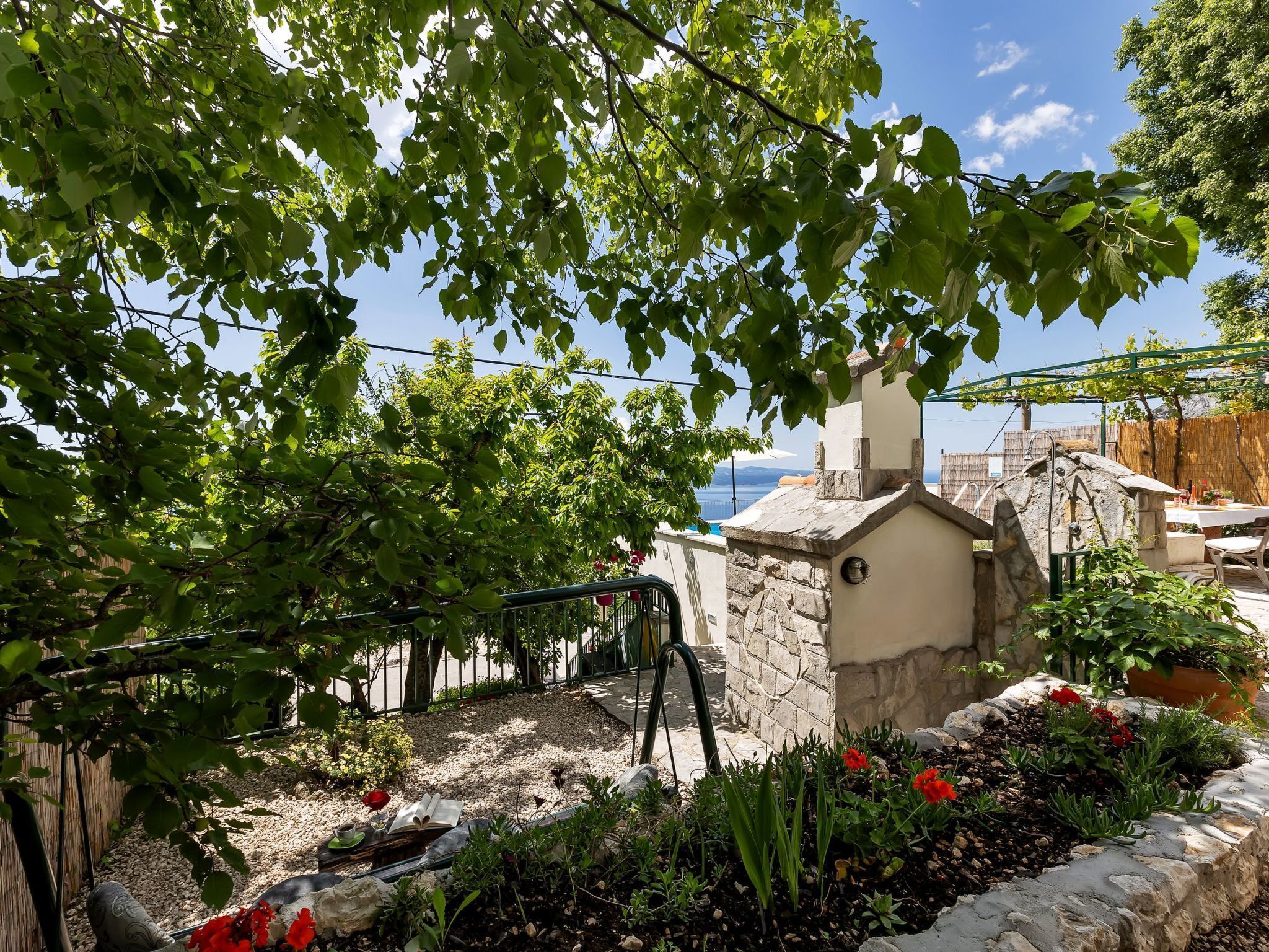 A garden with a stone structure, a table with a book and a cup, and a view of the sea.