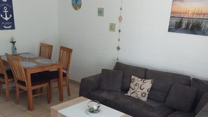A living room with a grey sofa, a wooden dining table with chairs, a coffee table, and a wall with decorative items and a picture. - in Tossens mit Schönem Garten by Interhome (Burhave)