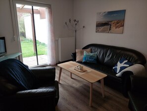 Ein Wohnzimmer mit schwarzem Ledersofa, einem Holztisch und einem Fernseher auf einem Lowboard.