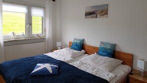 Een slaapkamer met twee bedden, witte beddengoed, een blauwe deken en kussens met strandmotieven.