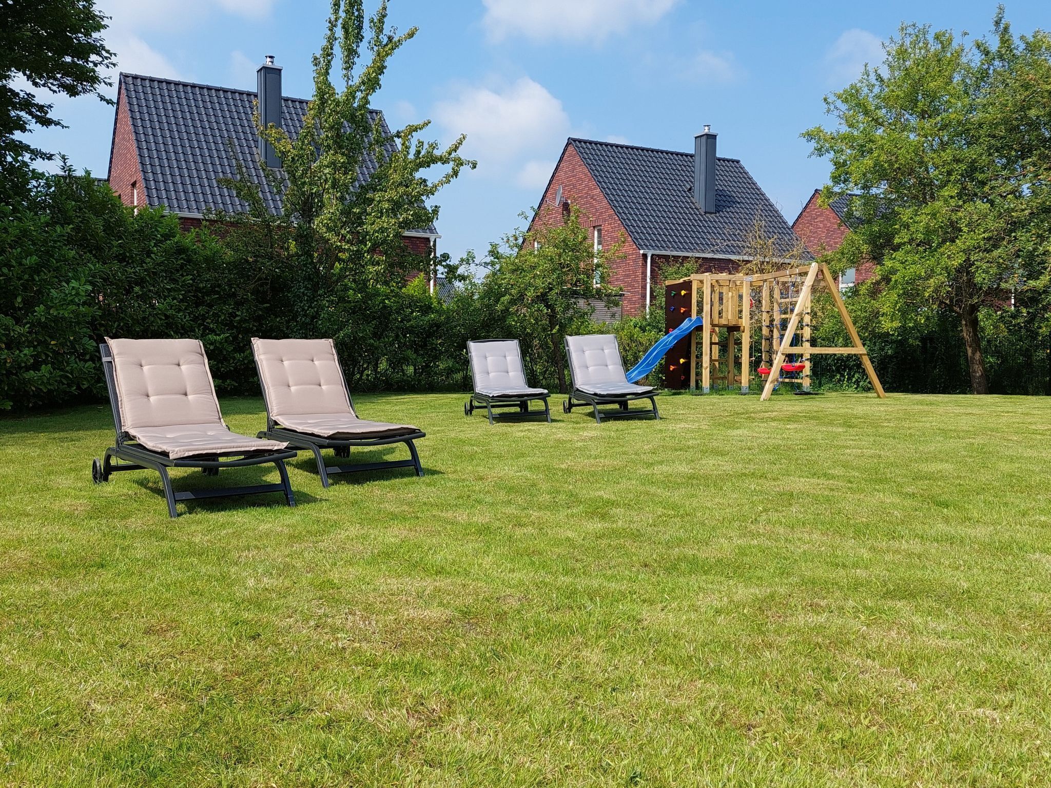 A grassy backyard with three lounge chairs and a wooden play structure.