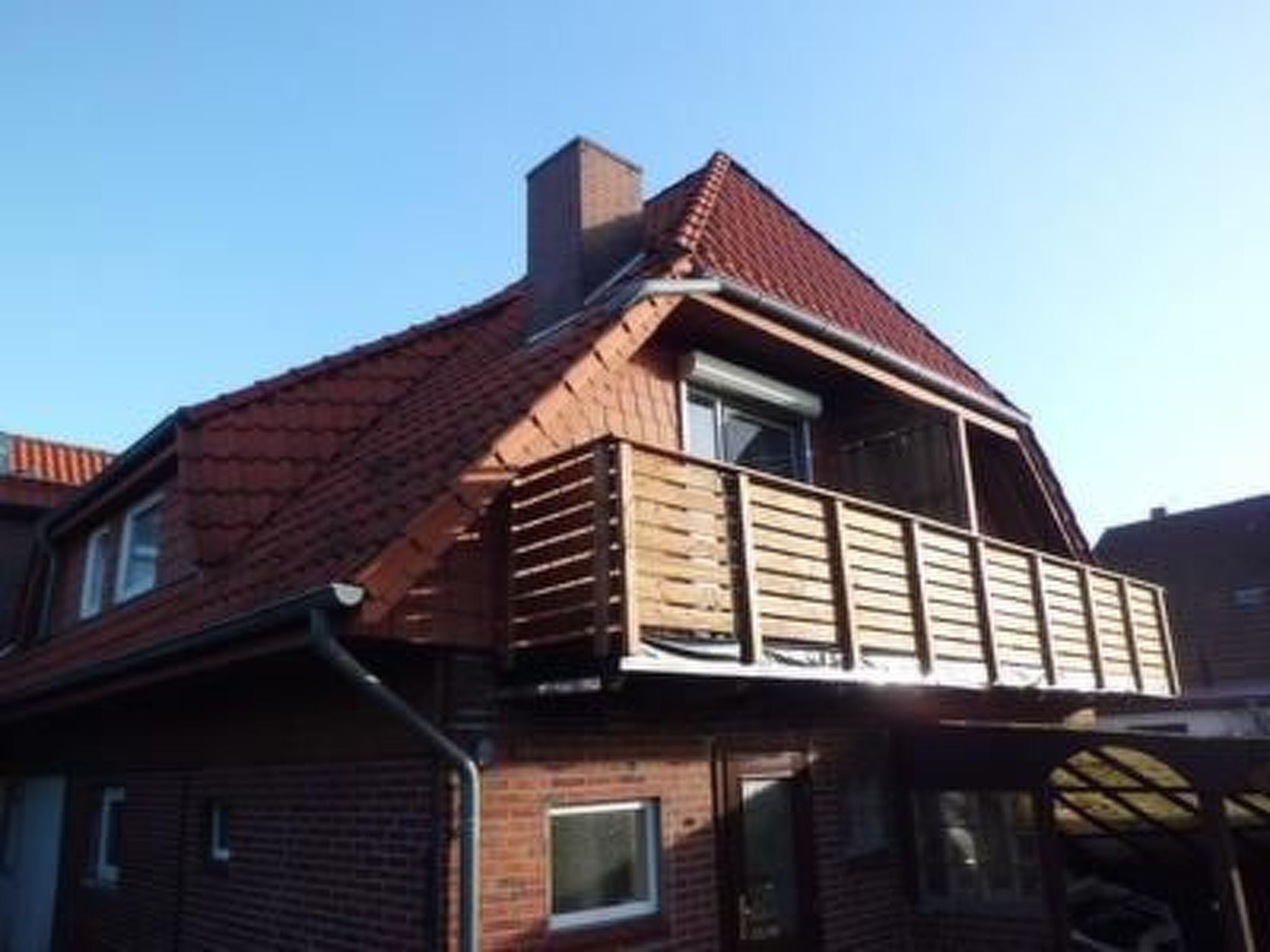 A two-story house with a red-tiled roof, a wooden balcony, and a brick facade.