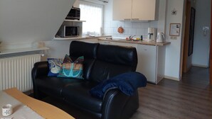 A compact living space with a kitchenette, a black leather sofa, and a small dining table. - Kajüte in Fedderwardersiel by Interhome (Burhave)