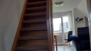 A wooden staircase leading to a second floor, a black chair, and a view of the outdoors through a glass door. - Kajüte in Fedderwardersiel by Interhome (Burhave)
