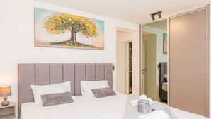 Ein Hotelzimmer mit einem großen Bett, einem Baumgemälde, einer Nachttischlampe und einem Spiegel.