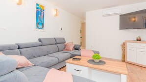 Ein modernes Wohnzimmer mit einem grauen Sofa, einem Holztisch und einem an der Wand befestigten Fernseher.
