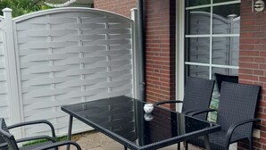 En uteplats med ett glasbord och två stolar, en mur av tegelsten och en grind av metall.