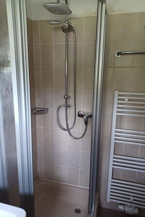 Une douche fermée par des parois en verre, dotée d’un pommeau de douche à main et d’un robinet mural.