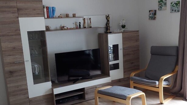 Ett modernt vardagsrum med en platt-TV, träskåp, en grå fåtölj och ett soffbord.