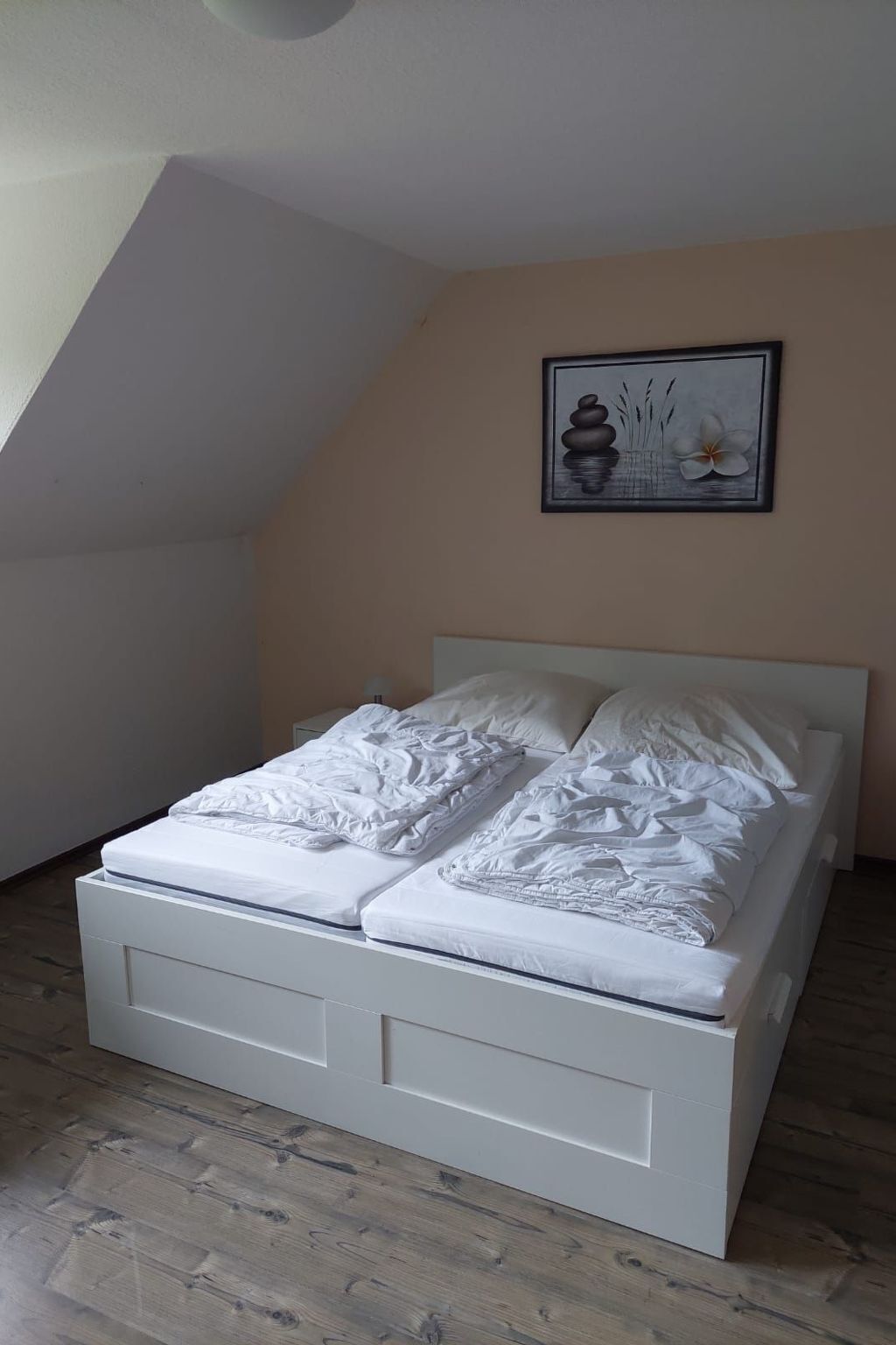 Un dormitorio con techo inclinado, una cama con ropa de cama blanca y un cuadro enmarcado en la pared.