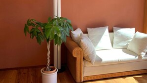 Quarto com sofá de vime, almofadas brancas e planta em vaso.