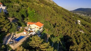 An aerial view of a hillside property with a large house featuring a red roof, a swimming pool, and a stone pathway leading to the house. - Privatwohnung mit Jacuzzi und Schwimmbad by Interhome (Split/Žrnovnica)