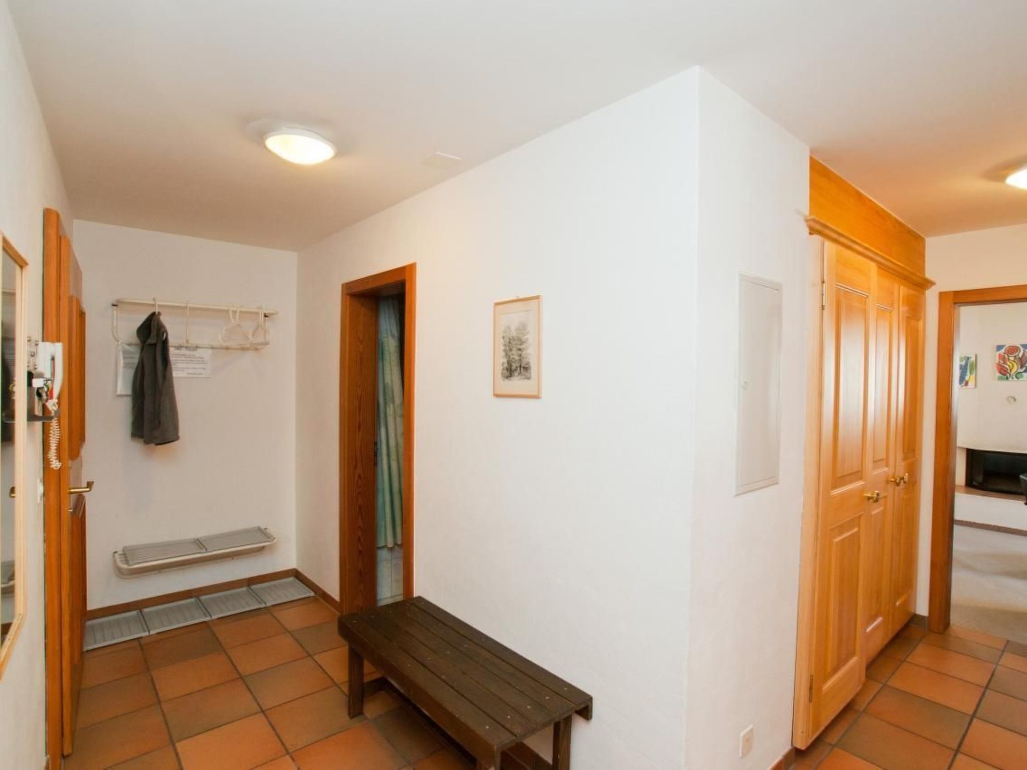 A small, clean room with a bench, a coat rack, and a door leading to another room.