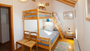 Een slaapkamer met een stapelbed, dakraam, houten meubels en een klein bureau met lamp.