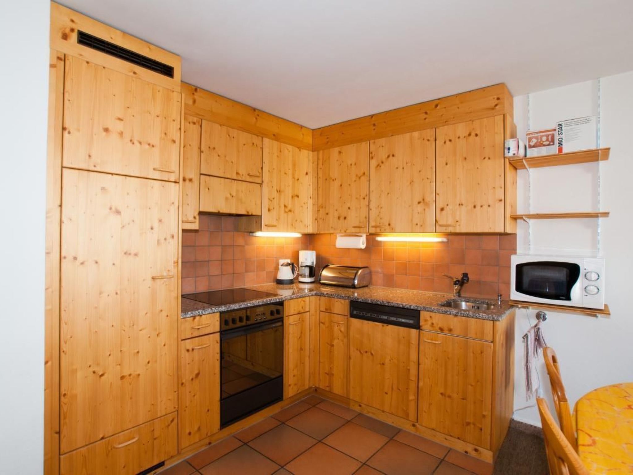 Een kleine keuken met houten kastjes, een inbouwoven, een magnetron en een koffiezetapparaat.