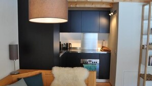 Pieni, käytännöllinen keittiö, jossa on tummat kaapit, puinen pöytä ja pehmeä, valkoinen tuoli.
