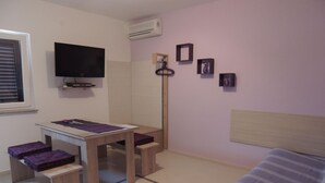 Een slaapkamer met een bed, een bureau met stoel, een televisie en een wandairconditioner.