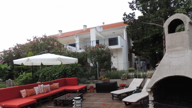 Een terras met een rode bank, lounge stoelen, een barbecue en een pizzaoven.
