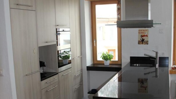 A modern kitchen with light wood cabinets, a black countertop, and a large island. - Chesa Madragena by Interhome (Pontresina)