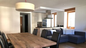 A modern kitchen with built-in appliances, a dining area with a wooden table and black chairs, and a grey sofa in the living area. - Chesa Madragena by Interhome (Pontresina)