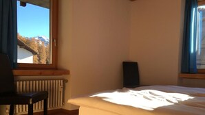 A bedroom with a wooden bed, a chair, a radiator, and a window with a view of mountains. - Chesa Madragena by Interhome (Pontresina)