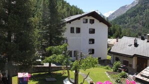 A white building with multiple windows, surrounded by a well-maintained lawn and trees, set against a mountainous backdrop. - Chesa Madragena by Interhome (Pontresina)