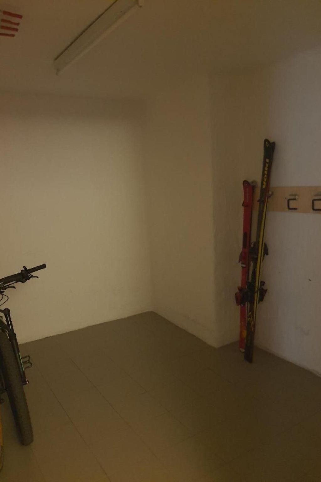 A room with a bicycle leaning against a wall, a pair of skis hanging on a rack, and a door with a number sign.