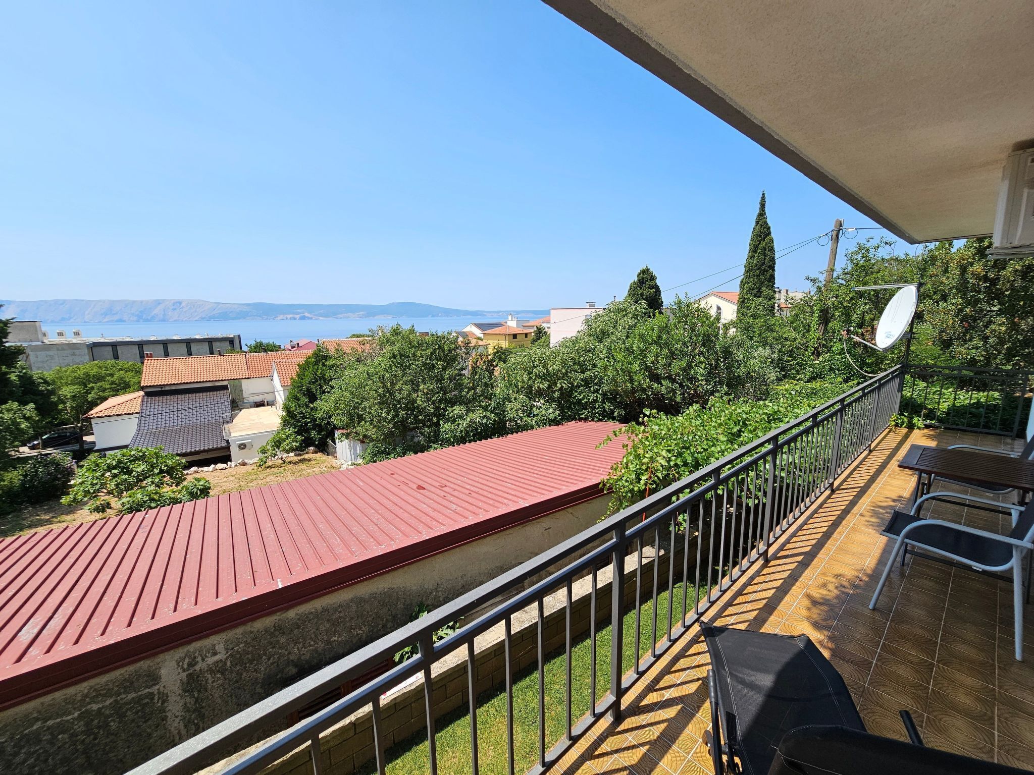 A balcony with a red roof, a view of the sea, and a satellite dish.