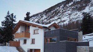 Una casa moderna de dos pisos con un balcón de madera, un garaje y vista a una montaña nevada.