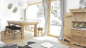Un salón luminoso y espacioso con una mesa de comedor de madera, un sofá y una mesa de centro. Hay una ventana grande con cortinas, y un mueble de madera con una bandeja encima.