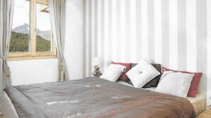 Un dormitorio con una cama, una ventana con cortinas y vistas a montañas.