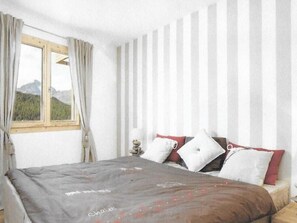 Ein Schlafzimmer mit Bett, einem Fenster mit Vorhängen und Blick auf Berge.