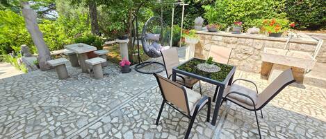 An outdoor patio with stone flooring, a table with chairs, and potted plants.