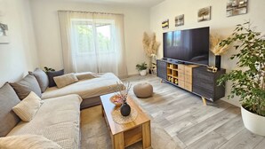 Una sala de estar moderna con sofá, mesa de centro, mueble para televisión y un ventanal con cortinas translúcidas.