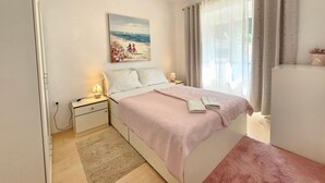 Un dormitorio con cama, mesitas de noche, una lámpara, un cuadro, una ventana con cortinas y vistas al exterior.