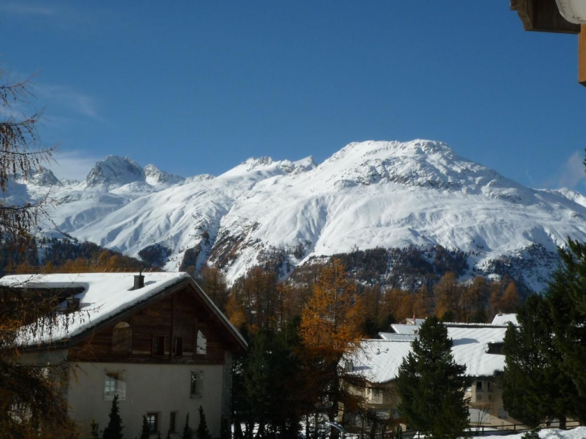 Ein Berggrundstück mit schneebedecktem Dach, umgeben von Bäumen und einem Hintergrund aus verschneiten Bergen.