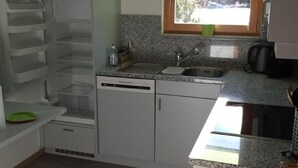A compact kitchen with white cabinets, a built-in dishwasher, a window with a view, and a granite countertop. - Chesa Azalea 3 klein by Interhome (Pontresina)