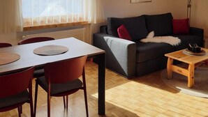 A modern living room with a dining table, red chairs, a grey sofa with a white throw, and a wooden coffee table. - Chesa Azalea 3 klein by Interhome (Pontresina)