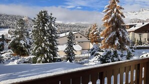 A snow-covered landscape with a wooden deck, snow-laden trees, and a mountain backdrop. - Chesa Azalea 3 klein by Interhome (Pontresina)
