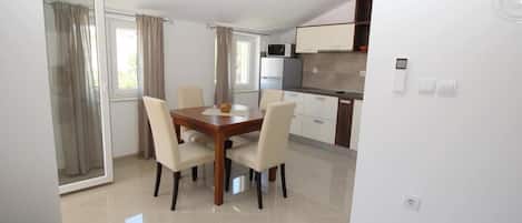 A modern kitchen with white cabinets, a microwave, and a stove. There is a dining area with a wooden table and four chairs.