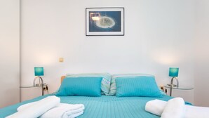 Ein ordentlich bezogenes Bett mit blauer Bettwäsche und weißen Handtüchern, zwei Nachttischlampen und ein gerahmtes Bild an der Wand.
