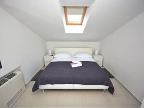 Ein Schlafzimmer mit Dachfenster, einem Bett mit weißer Bettwäsche, einem Nachttisch mit Lampe und einem Heizgerät.