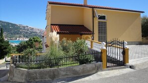 A yellow building with a red-tiled roof, a gated entrance, and a view of a mountainous landscape. - Appartement in Baška mit Eigener Terrasse by Interhome (Krk/Baška)