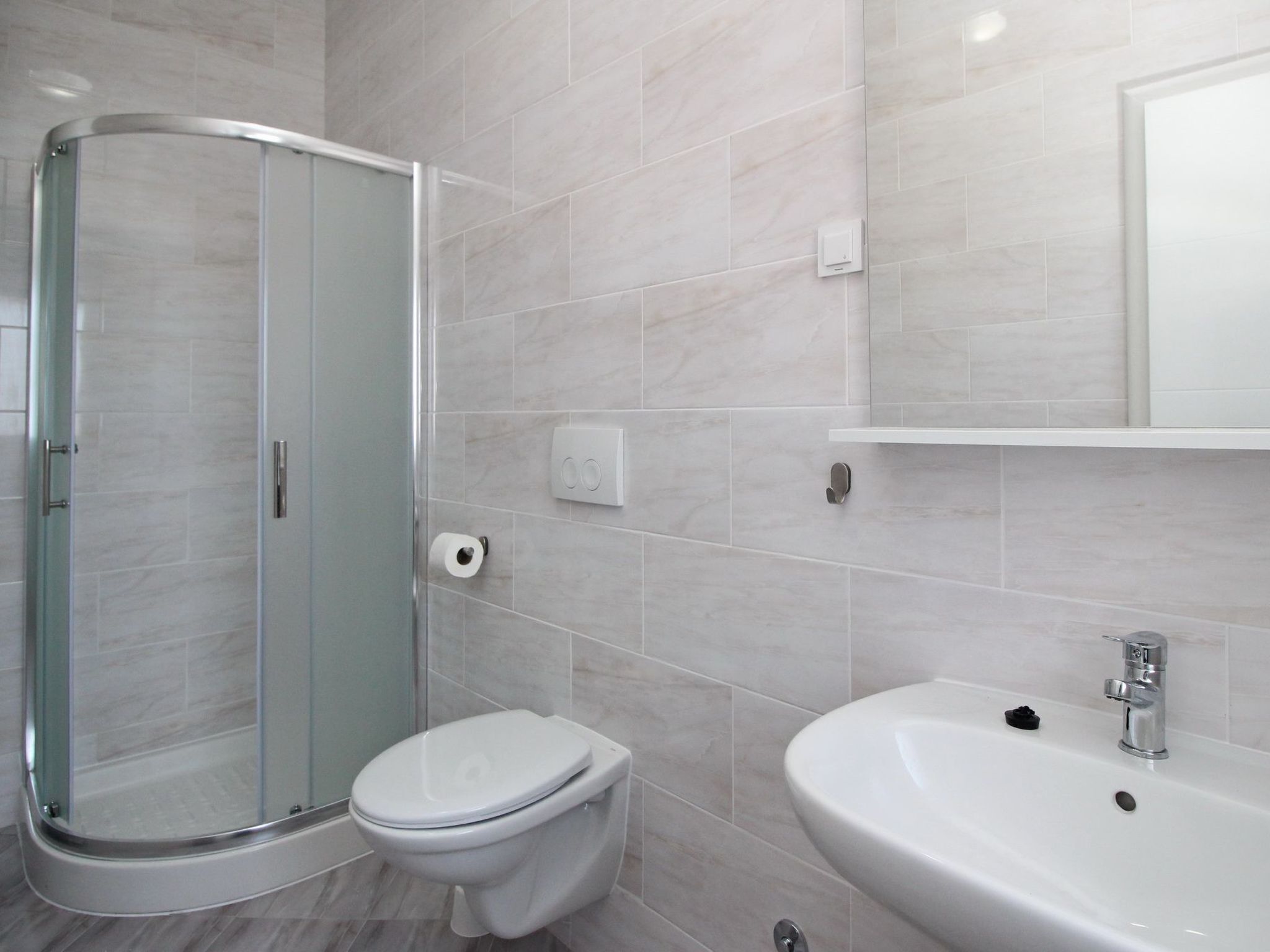 A modern bathroom with a glass shower enclosure, a toilet, and a sink with a mirror above.