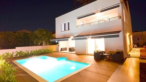 Et moderne hus med to etager, swimmingpool og udendørs siddeområde.