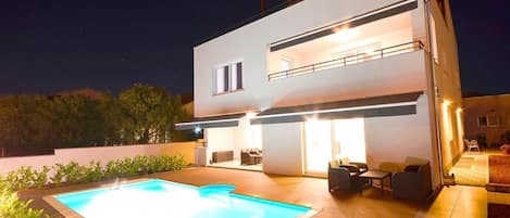 A modern two-story house with a swimming pool and outdoor seating area.