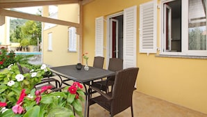 Un patio al aire libre con una mesa y sillas, rodeado de muros amarillos y contraventanas blancas.
