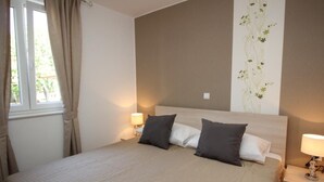 Una cama bien hecha con cabecera, dos lámparas de noche y una ventana con cortinas.